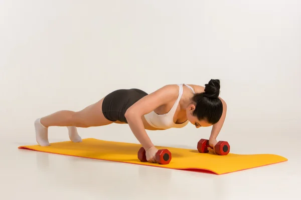 Sterke jonge vrouw doet push ups oefening met halters. — Stockfoto