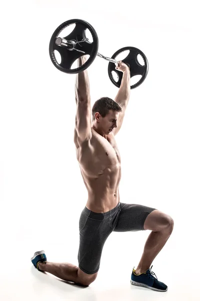 Muscular man standing on knee, holding barbell over his head — 스톡 사진