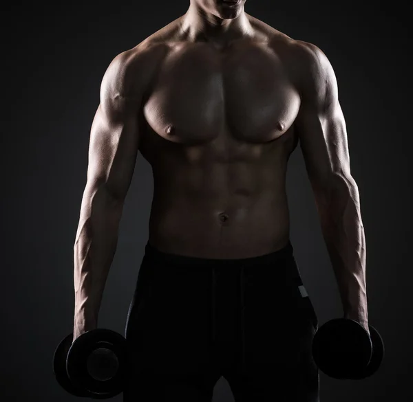 Мускулистый мужчина показывает идеальное тело с гантелями на черном фоне — стоковое фото