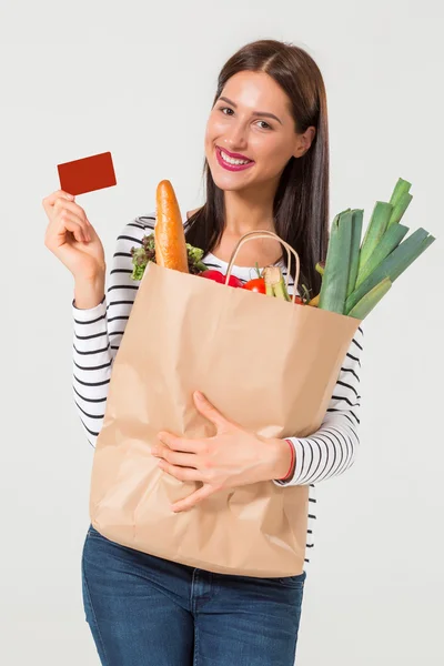 Mujer joven con tarjeta de crédito sosteniendo comestibles —  Fotos de Stock