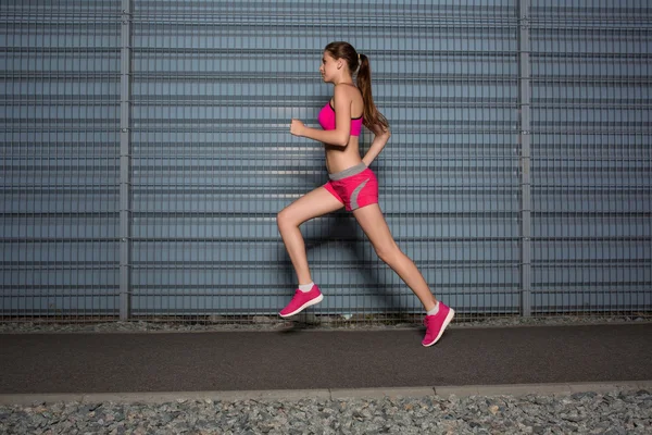 Uma mulher em fuga. jogging contra o fundo de uma parede cinza — Fotografia de Stock