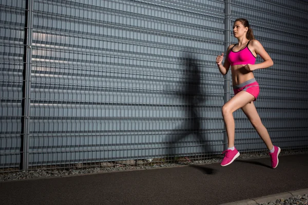 दौड़ने वाली महिला। एक ग्रे दीवार की पृष्ठभूमि के खिलाफ जॉगिंग — स्टॉक फ़ोटो, इमेज