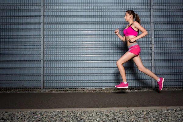 Uma mulher em fuga. jogging contra o fundo de uma parede cinza — Fotografia de Stock