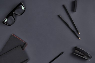 İki siyah not defteri, gözlükler, kalemler ve koyu gri arka planda zımba. Kırtasiye, ofis ya da eğitim için malzeme. Kapat, boşluğu kopyala