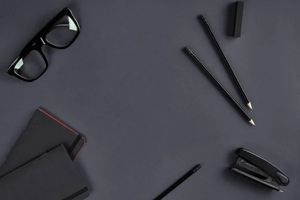 Deux blocs-notes noirs, lunettes, crayons et agrafeuse sur fond gris foncé. Papeterie, fournitures de bureau ou d'enseignement. Fermer, copier l'espace — Photo