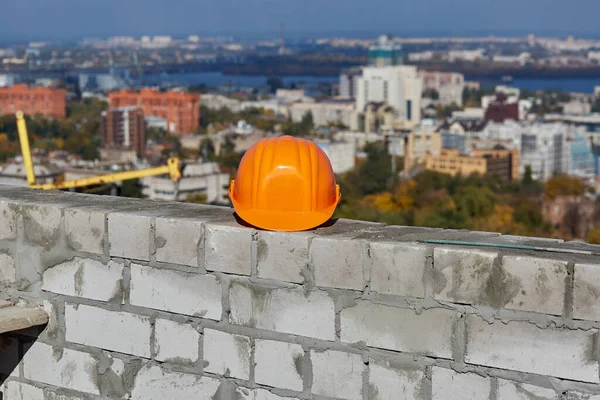 Le casque orange est sur un mur de briques. Toit du bâtiment moderne en construction. Paysage urbain panoramique pittoresque, ciel bleu, journée ensoleillée — Photo