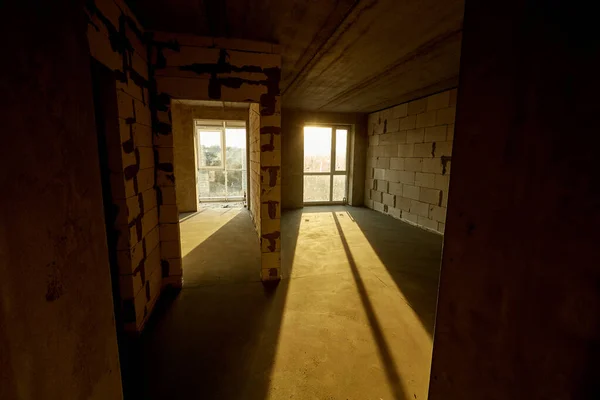 Unfinished empty flat, two huge plastic windows, walls made of aerated concrete blocks, cement screed on the floor. Building under construction