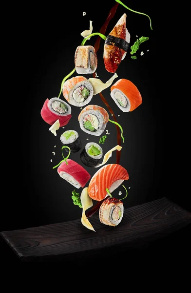 Sushi s ozdobami a sójovou omáčkou vznášející se nad talířem na černém pozadí — Stock fotografie