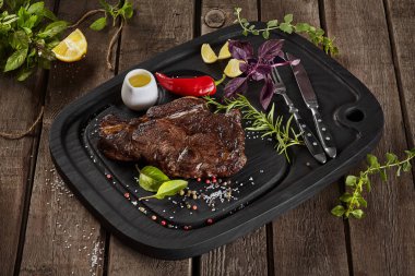 Baharatlı ızgara dana biftek ve ahşap arka planda çatal bıçak.