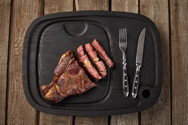 Ovanifrån av skivad kalvkött entrecote på svart bräda med bestick — Stockfoto