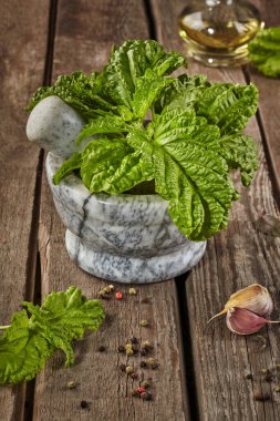 Kıvırcık fesleğenli taş havan ve ahşap masadaki baharatlar.