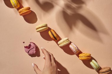 Kadın eli bej arka planda ısırılmış makarona uzanıyor.