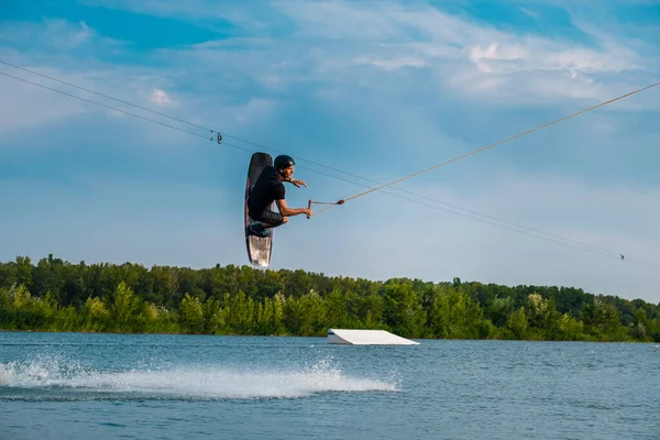 Чоловік-водій стрибає над водою з дошкою тримає мотузку — стокове фото