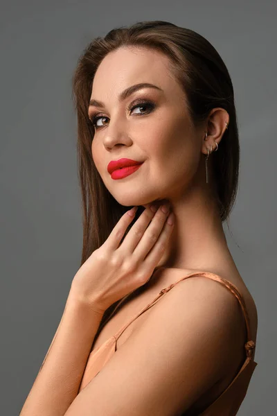 Mulher morena em vestido bege de seda. Sorrindo e tocando seu pescoço, posando de lado contra fundo cinza. Fechar — Fotografia de Stock