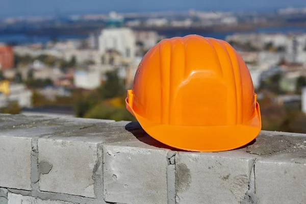 Chapeau dur en plastique orange est sur un mur de briques. Toit du bâtiment moderne en construction. Paysage urbain panoramique panoramique, ciel bleu, journée ensoleillée — Photo