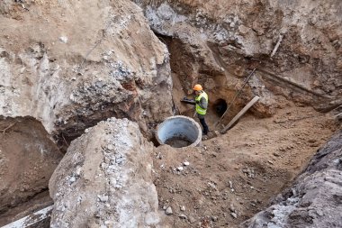 İşçi, inşaat halindeki yeni bir gökdelenle iletişim kurmak için kazı çukurunda kürekle siper kazıyor.