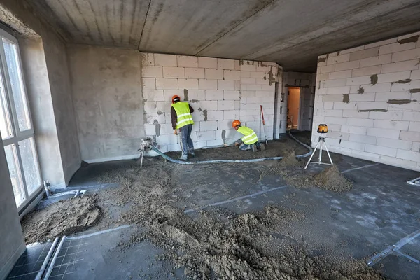 Двоє робітників використовують пневматичний конвеєр і тахометр в квартирі будівлі, що будується. Підготовка до виготовлення цементної стяжки підлоги — стокове фото