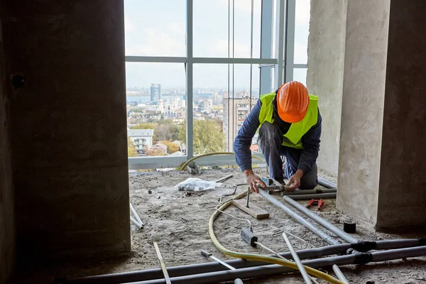 Constructeur professionnel en vêtements de travail et casque de sécurité installant des tuyaux en plastique à l'aide d'outils modernes dans l'appartement du bâtiment en construction — Photo