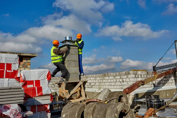 Deux travailleurs portant des casques de sécurité travaillent avec un système de ventilation sur le toit du bâtiment en construction. Paysage urbain panoramique, console pour berceau — Photo