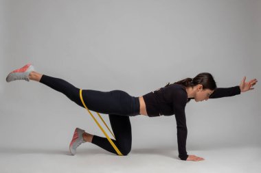 Gri arka planda direniş bandıyla Dandayamana Bharmanasana yapan kadın.