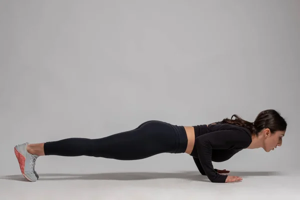 Vrouw in zwarte sportkleding doet push-ups op grijze achtergrond — Stockfoto