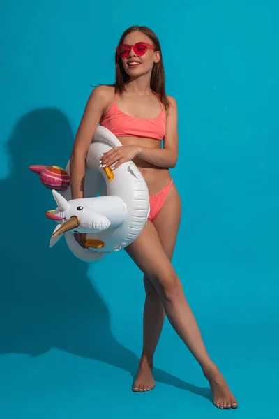 Joyful meisje in bikini en zonnebril met zwemring op blauwe achtergrond — Stockfoto