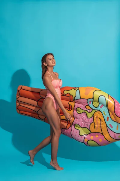 陽気女の子で水着持ってインフレータブルマットレス上の青の背景 — ストック写真