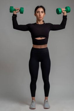 Fit esmer, gri arka planda dambıl omuz presi yapıyor.