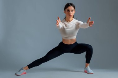 Sportif kız gri arka planda vücut ağırlığı ile yan yana çömelme hareketleri yapıyor.