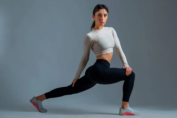 Menina realizando lunge para a frente com torção do corpo no fundo cinza — Fotografia de Stock