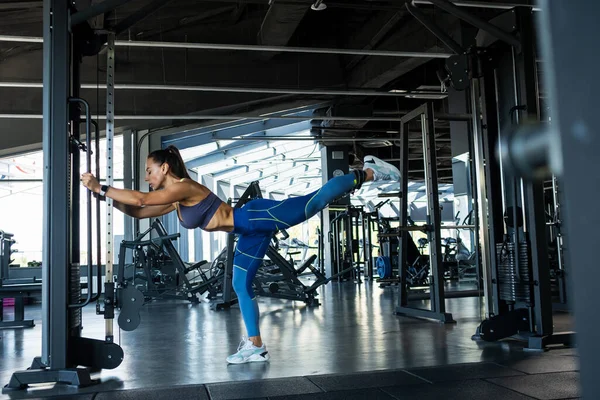 Sportif kız spor salonunda kablolu yayında kalça uzantısını yapıyor. — Stok fotoğraf