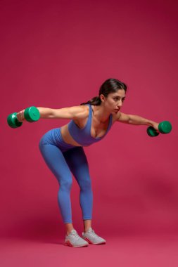 Atletik kız, kestane rengi arka planda omuz egzersizi yapıyor.