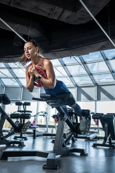 Junge Frau macht Hyperextension mit Hantelscheibe im Fitnessstudio — Stockfoto