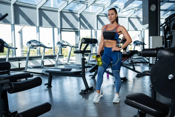 Spor salonunda elinde su şişesiyle duran atletik kız. — Stok fotoğraf