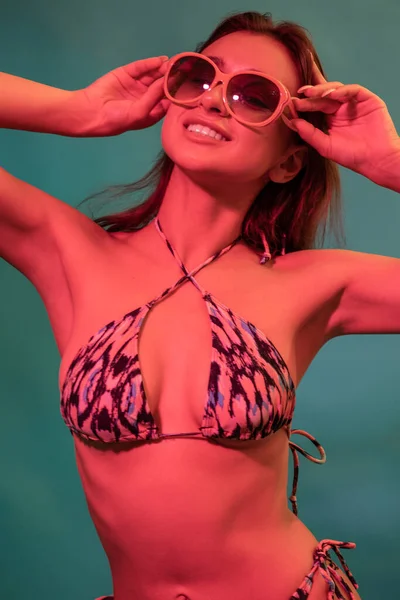 Smiling girl in swimsuit and sunglasses posing on blue background — Stock Photo, Image