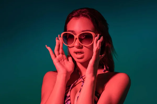 Verrast meisje in badpak en zonnebril op turquoise achtergrond — Stockfoto