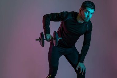 Atletik adam dambılla omuz egzersizi yapıyor.
