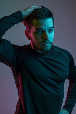 Siyah uzun kollu spor gömlekli genç adam saçına dokunuyor.