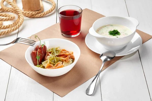 Mittagessen mit Okroshka, gekochte Farfalle mit Würstchen, Beerengetränk — Stockfoto