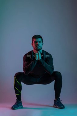 Atletik genç adam dambıl sumo yapıyor.