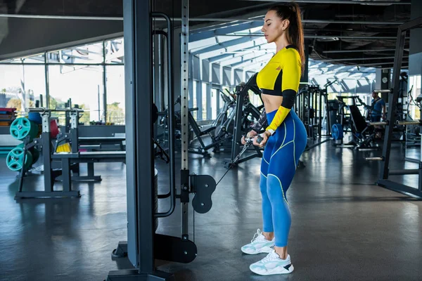 Sporty girl doing biceps curl on cable crossover at gym — Stockfoto