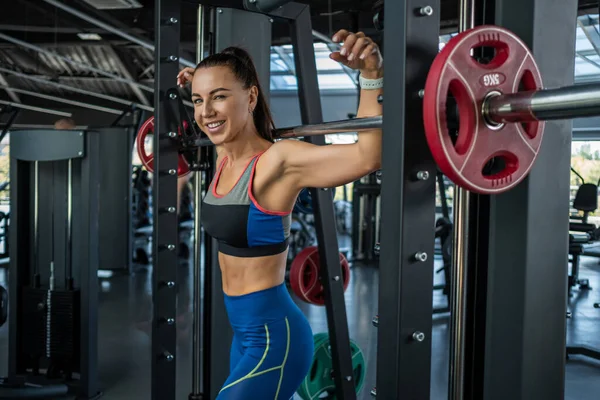 Cheerful fit young brunette standing near Smith machine at gym — Stockfoto