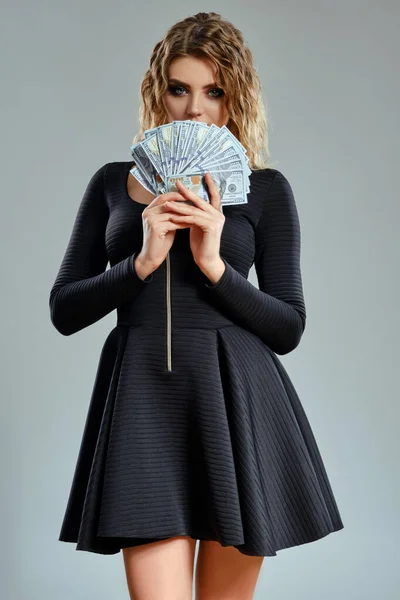 Blondes Mädchen in schwarzem kurzen Kleid hält etwas Bargeld in der Hand und posiert vor grauem Hintergrund. Glücksspiel, Poker, Casino. Nahaufnahme. — Stockfoto
