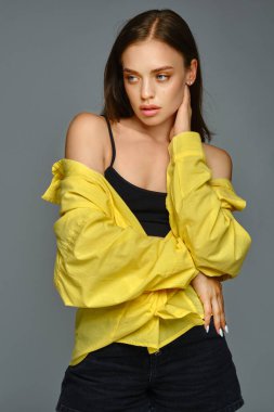 Gri arka planda eli boynuna dokunan düşünceli genç bir kadın.