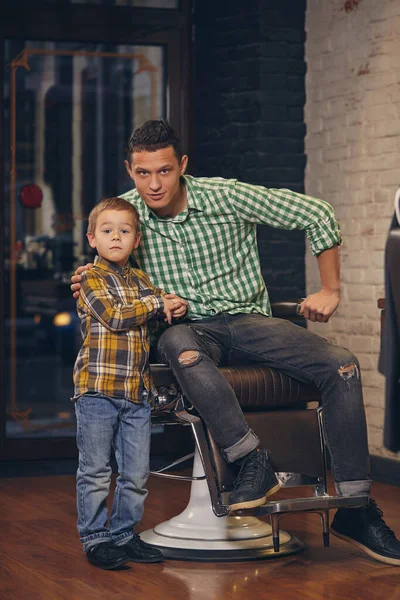 Jovem pai bonito e seu pequeno filho elegante na barbearia à espera de barbeiro — Fotografia de Stock