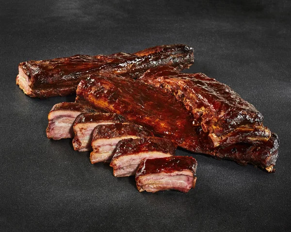 Sliced grilled pork ribs in barbecue sauce on stone surface — Stock Photo, Image