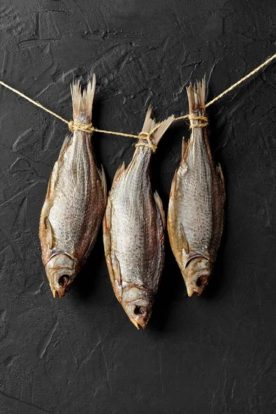 Getrockneter gesalzener Rotaugen-Fisch hängt am Seil an schwarzer Wand — Stockfoto