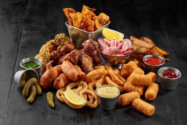 Set of savory beer snacks on black wooden table with condiments clipart