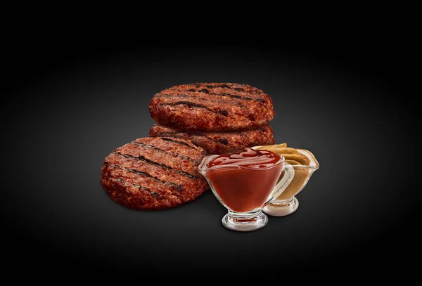 Ψητές κοτολέτες burger με δύο σάλτσες σε διάφανες βαρκούλες σε μαύρο φόντο. Κρέας ψητό στη σχάρα μπάρμπεκιου. Κλείσε. — Φωτογραφία Αρχείου