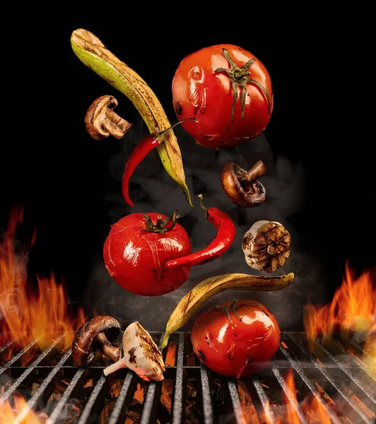 Grilled tomatoes, zucchini, chili, champignons, halves of garlic are falling down on black background. Barbecue, fire, charcoal and smoke. Close up — Stock Photo, Image